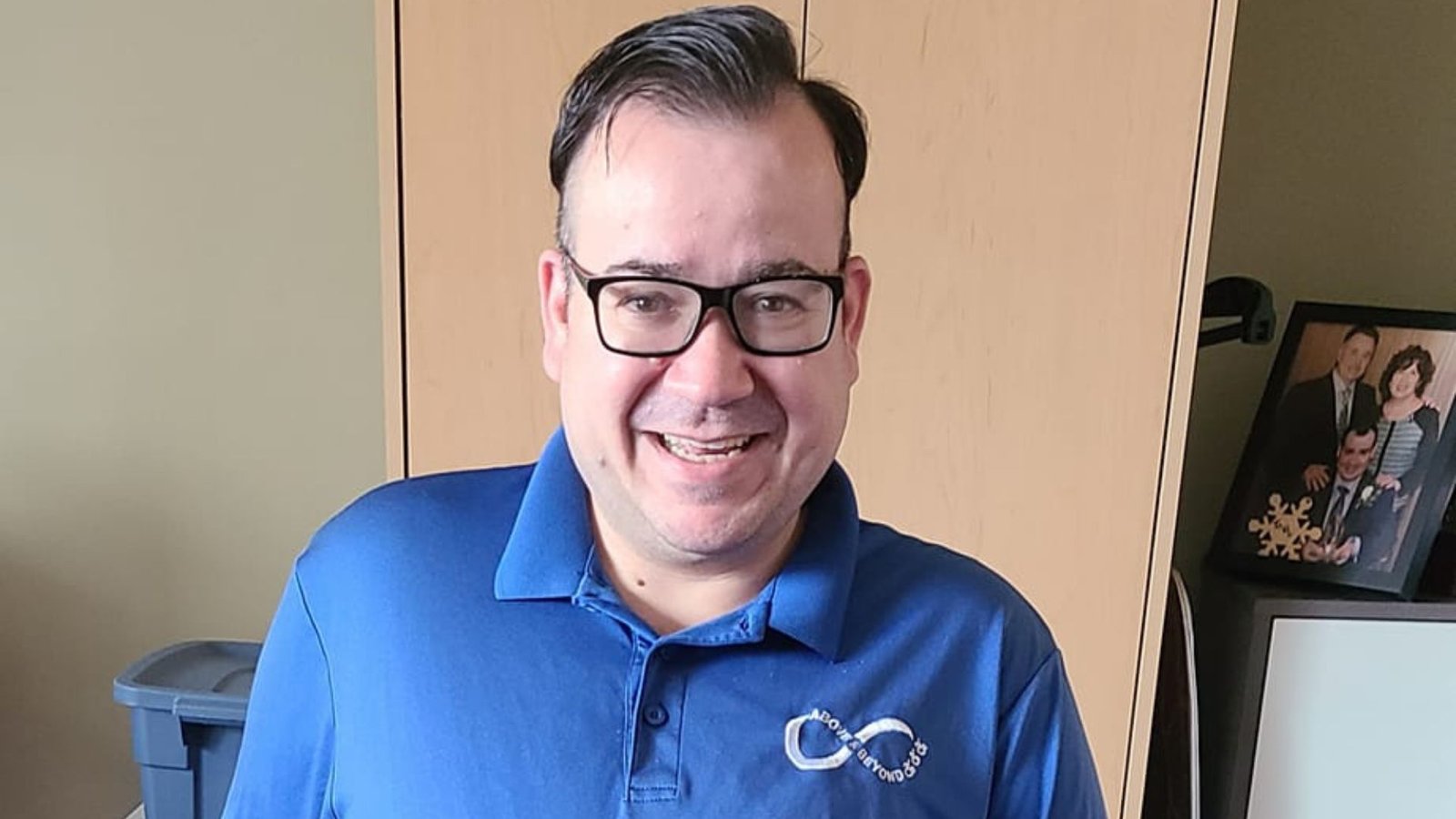 Anthony smiling wearing a blue shirt and glasses in his wheelchair.